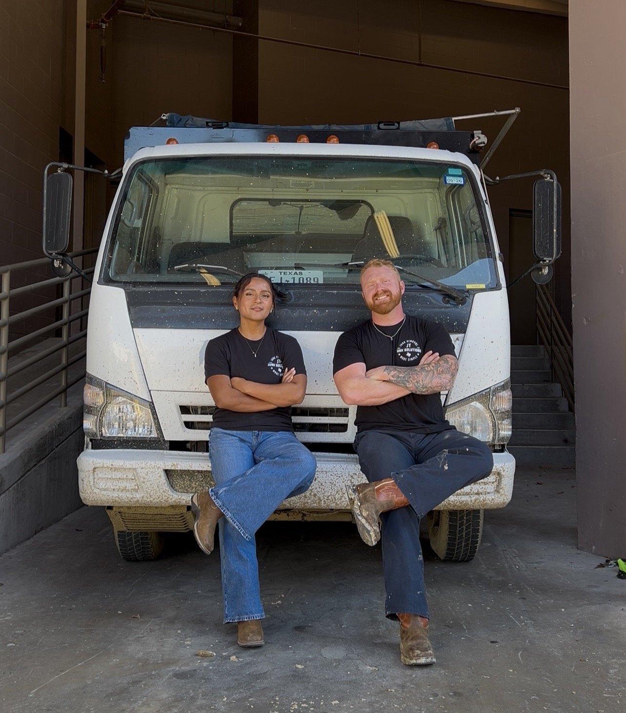 Tanner and Jackie, the owners of JT Junk Solutions, seated on the front bumper of their truck